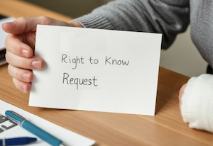 An injured person in a bandage holding up a sign with the words "right to know request" sitting at a desk 